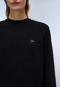 Čierna dlhá rukávová košeľa vyrobená z bavlny, s okrúhlym výstrihom a malým vyšitým logom na hrudníku. Hladká textura, voľný strih.