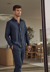Donkerblauwe linnen blouse met lange mouwen en knoopsluiting, gecombineerd met bijpassende linnen broek, beide met een relaxte pasvorm en een soepele textuur.