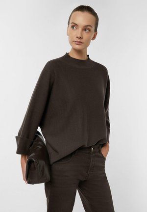 Brązowy sweter z dzianiny z wysokim kołnierzem i oversize'owymi rękawami, w połączeniu z ciemnobrązowymi dopasowanymi jeansami oraz brązową skórzaną torbą.