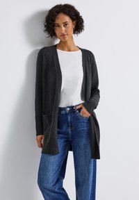 Donkergrijze cardigan met ribbels bij de mouwen en zakken, gedragen over een wit shirt en blauwe high-waisted jeans. Gladde textuur, open voorkant ontwerp.