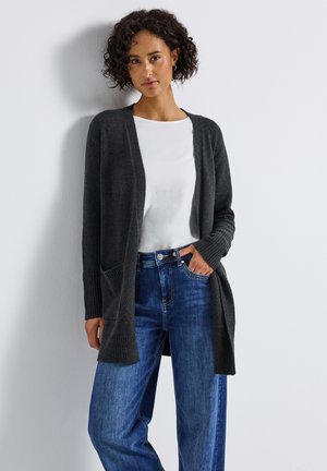 Dunkelgrauer Cardigan mit gerippten Ärmeln und Taschen, getragen über einem weißen Shirt und blauen High-Waisted-Jeans. Glatte Textur, offenes Frontdesign.