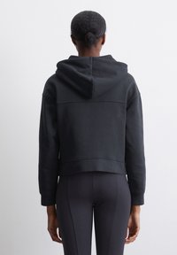 Sudadera negra cortada con una gran capucha, hecha de una tela suave. Presenta un diseño simple y detalles de costura, combinada con leggings negros.