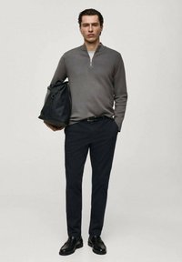 Grå zip-up tröja, mörka byxor, svarta skor, håller en svart väska. Slät textur, smal passform, avslappnad design. Enkel färgpalett.