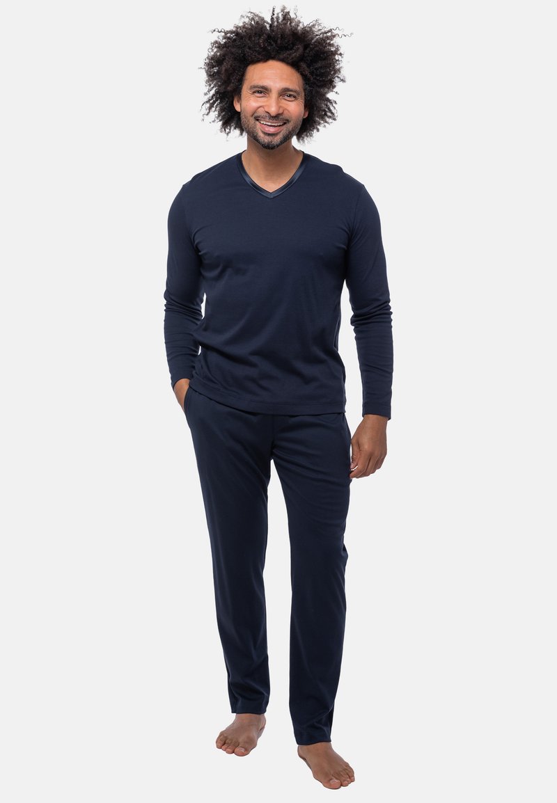 Navyblauwe longsleeve V-hals top en bijpassende broek van zachte stof; slim fit met een subtiele textuur, model staat blootsvoets.