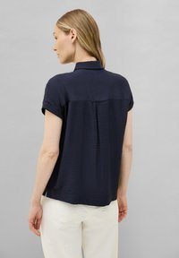 Camicia blu navy a maniche corte con colletto e tessuto testurizzato, caratterizzata da una piega centrale sul retro e una vestibilità rilassata.