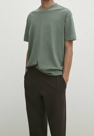 Light green cotton t-shirt with a crew neckline, relaxed fit, and short sleeves, paired with dark brown trousers with pockets.