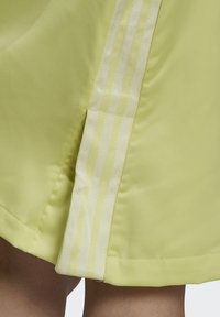 Zbliżenie żółto-zielonej tkaniny z satynowym pionowym paskiem na odzieży w pobliżu dołu, nad nogami osoby.