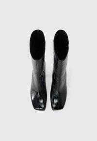 Μαύρα δερμάτινα μποτάκια αστραγάλου με ψηλό, στενό κορμό και μυτερές μύτες. Η επιφάνεια έχει γυαλιστερό φινίρισμα με ελάχιστες ραφές.
