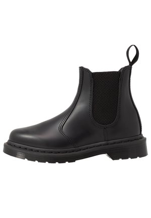 Botín Chelsea negro con cuero brillante y suave, paneles laterales elásticos y suela de goma plana, diseñado para el estilo y la comodidad.