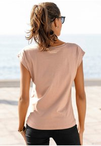 Light pink cotton t-shirt with short sleeves, rounded neckline, and a small "Venice Beach" print on the back, paired with black pants.