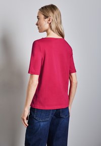 Úzké tričko s krátkým rukávem v jasně růžové barvě z bavlny, s kulatým výstřihem a hladkou texturou, spárované s volnými tmavými džínovými kalhotami.