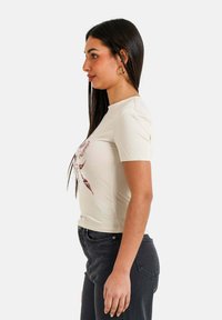 Camiseta de manga corta color crema con diseño gráfico en rojo, combinada con jeans oscuros. Corte simple, textura suave y escote redondo.