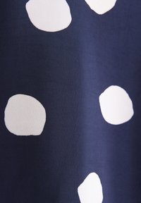 Tissu bleu marine avec de grands pois blancs irréguliers, montrant la texture et de légères rides dans le matériau.