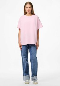 T-shirt oversize pink con maniche corte, abbinato a jeans in denim azzurro chiaro con orli sfilacciati e una vestibilità comoda.