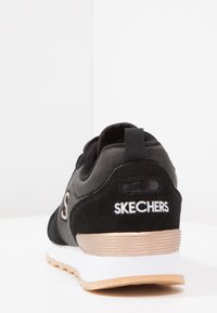 Czarny but sportowy z materiału zamszowego i siateczkowego, z teksturowanym obcasem, białymi i złotymi akcentami oraz wyraźnym logo "SKECHERS".