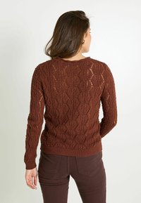 Pull en tricot marron avec un motif de dentelle texturé, manches longues et encolure ronde, associé à un pantalon marron assorti.