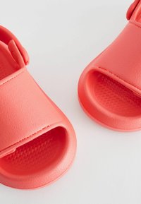 Korallfarvede sandaler med åben tå lavet af tekstureret plastik, med en flad sål og justerbar rem på siden for en sikker pasform.
