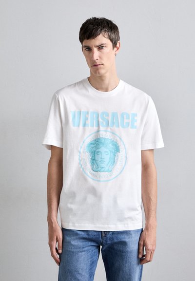 Hvid bomulds t-shirt med lys blå "VERSACE" tekst og et centreret medusa grafik. Korte ærmer, crew neck, afslappet pasform, minimalistisk design.