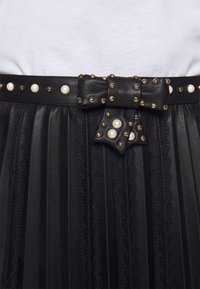 Cinturón de cuero negro con pliegues y hebilla en estilo lazo, adornado con tachuelas doradas y acentos de perlas, con detalles de encaje en los bordes.