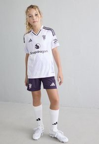 Hvit fotballtrøye med lilla detaljer, med v-hals, Adidas-logo og sponsormerking. Kombinert med lilla shorts og hvite sokker.
