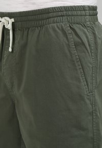 Shorts in cotone verde con vita elastica e dettaglio con cordoncino; presenta tasche laterali e una texture liscia e opaca.