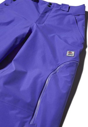 Lilla veekindlad püksid siledast kangast, millel on lukuga tasku ja bränditud silti, esikinnitusnuppude ja vöölusikatega.