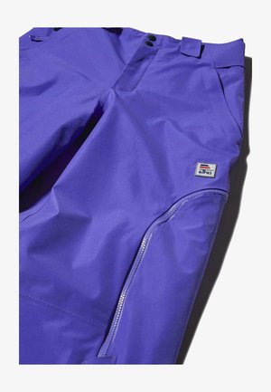 Lilla veekindlad püksid siledast kangast, millel on lukuga tasku ja bränditud silti, esikinnitusnuppude ja vöölusikatega.