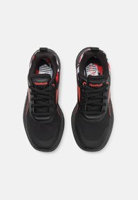 Baskets de sport noires avec des panneaux en maille et des accents rouges. Présentent un col rembourré, un système de laçage à l'avant et une semelle en caoutchouc texturée. Logo Reebok présent.