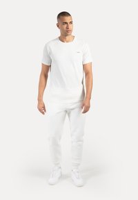 Camiseta de algodón blanca con mangas cortas, cuello redondo y diseño minimalista. Combinada con pantalones deportivos blancos a juego y zapatillas blancas.