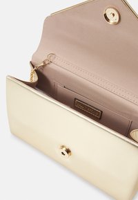 Pochette métallique dorée au toucher lisse, dotée d'une fermeture à tourniquet et d'une doublure intérieure beige avec une étiquette de marque.