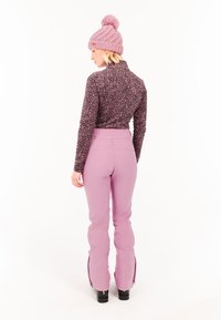 Mikina z fleecu s leopardím vzorom, ružové lyžiarske nohavice a pletená ružová čiapka s pom-pomom. Nohavice majú bočné zipsy a vysoký pás.