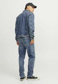 Jachetă din denim și blugi de culoare albastru deschis, croială clasică; jacheta are închidere cu nasturi și buzunare pe piept; adidași negri cu talpă și șireturi albe.