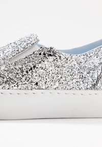 Sömlös skofodrad med silverglitter och vit sula, samt ett elastiskt panel på ovansidan för enkel användning.