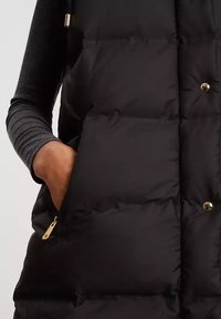Czarna kamizelka puchowa o pikowanej konstrukcji, z złotymi detalami i bocznymi kieszeniami. Materiał wydaje się być miękki i termoizolacyjny.