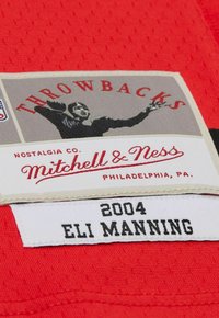 Throwbacks Mitchell & Ness label on red fabric showing a football player silhouette and "2004 ELI MANNING" text.