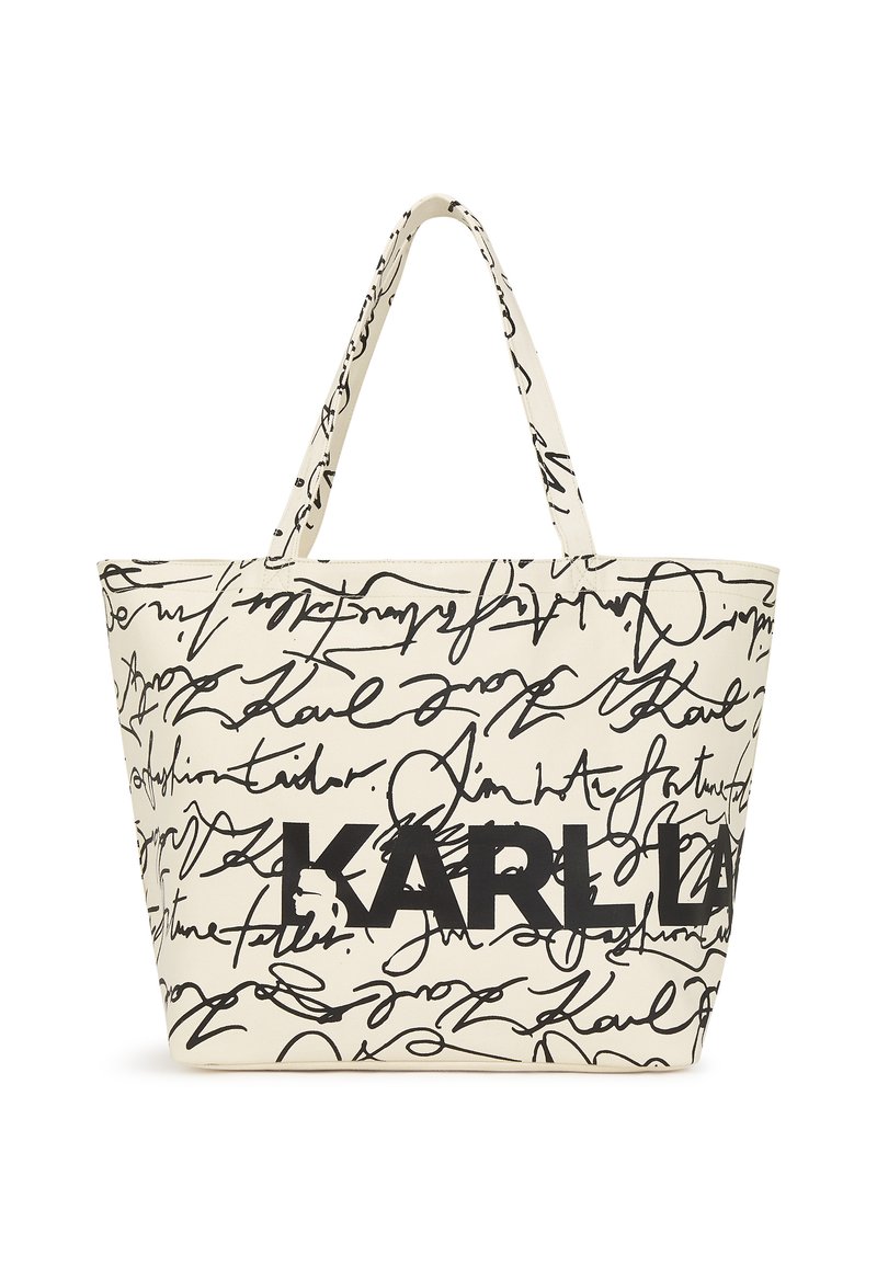 Beige Stofftragetasche mit schwarzem handgeschriebenem Text und einem auffälligen "KARL"-Logo. Das Design umfasst eine geräumige, strukturierte Form und zwei Griffe.