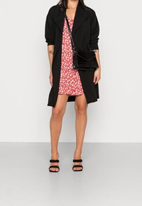 Sort åben frakke med åbent front over en rød blomsterkjole, kombineret med sorte teksturerede slingback-hæle og en sort crossbody-taske med krokodilleprint.