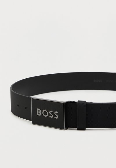 Ceinture noire avec une texture lisse et mate, dotée d'une boucle rectangulaire en argent gravée du mot "BOSS". Réglable grâce à plusieurs trous.