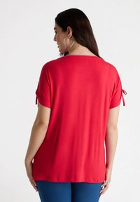 Top rojo de manga corta con un ajuste holgado, detalles acentuados atados en las mangas y una textura suave, combinado con pantalones azules.