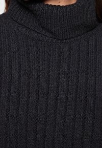 Schwarzer Strickpullover mit hohem geripptem Rollkragen und vertikaler Textur, der ein weiches, kuscheliges Material präsentiert.