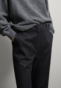 Grijze gebreide trui met geribde manchetten, gecombineerd met donkere, gestructureerde broeken met een lichte glans en zijzakken. Zachte, casual look.