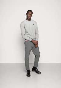 Grå sweatshirt med rund halsudskæring og broderet logo, parret med grå skrædderbukser og sorte snørebåndssko. Minimalistisk design.