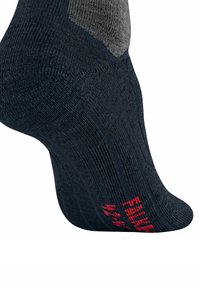 Calzino grigio scuro caratterizzato da un design a maglia testurizzata, tacco imbottito e branding rosso sul lato. Il materiale appare morbido e flessibile.