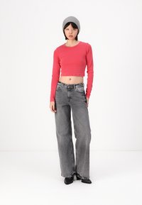 Rozā īsā jaku ar garām piedurknēm apvieno ar augsto jostasvietu, brīvi pieguļošām pelēkām džinsām. Modelis valkā pelēku cepuri un melnu apavu.