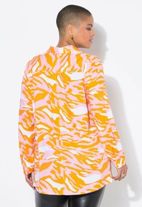 Chemise à manches longues ornée d'un motif rayé tigre rose et orange, réalisée en tissu lisse avec un col et une fermeture à boutons.