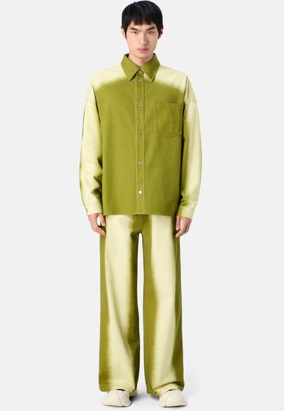 Camisa oversized en degradado verde y beige con cuello de botón y bolsillo frontal, combinada con pantalones de pierna ancha a juego. Tejido texturizado.