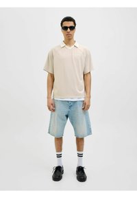 Beige kortærmet polo t-shirt med hvid krave, parret med lyseblå denim shorts. Sorte sko og stribede hvide sokker fuldender looket.