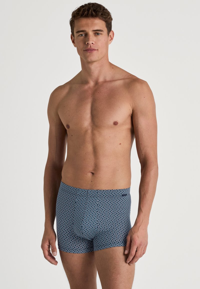 Mannen zwemshorts in marineblauw met een witte golfpatroon. Gemaakt van rekbare stof, met een aansluitend ontwerp en een elastische tailleband.