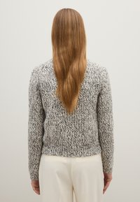 Suéter de punto en gris y blanco con un patrón texturizado, de mangas largas y con un dobladillo acanalado, combinado con pantalones color crema.