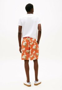 Shorts naranjas florales con una tela ligera, que presentan un patrón floral blanco y un corte relajado. Combinados con una camiseta blanca sencilla y zapatos casuales.